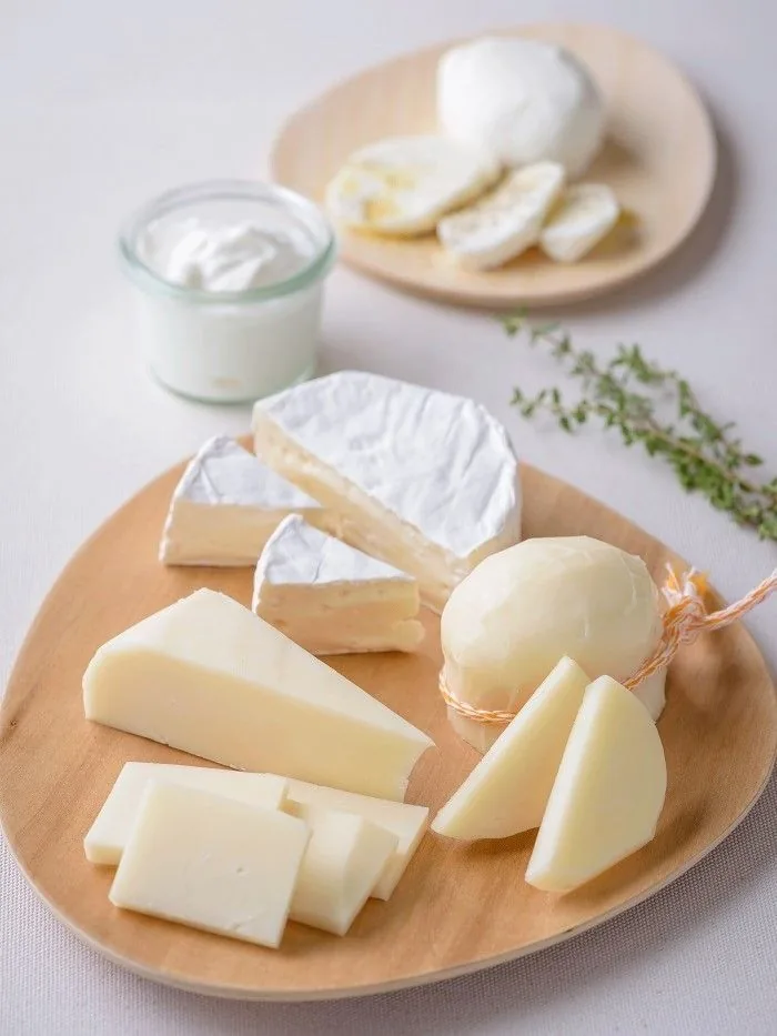 Tagliere di legno con i formaggi della fattoria: scamorza, fette di latteria, una punta a pasta molle e una ciotola di yogurt