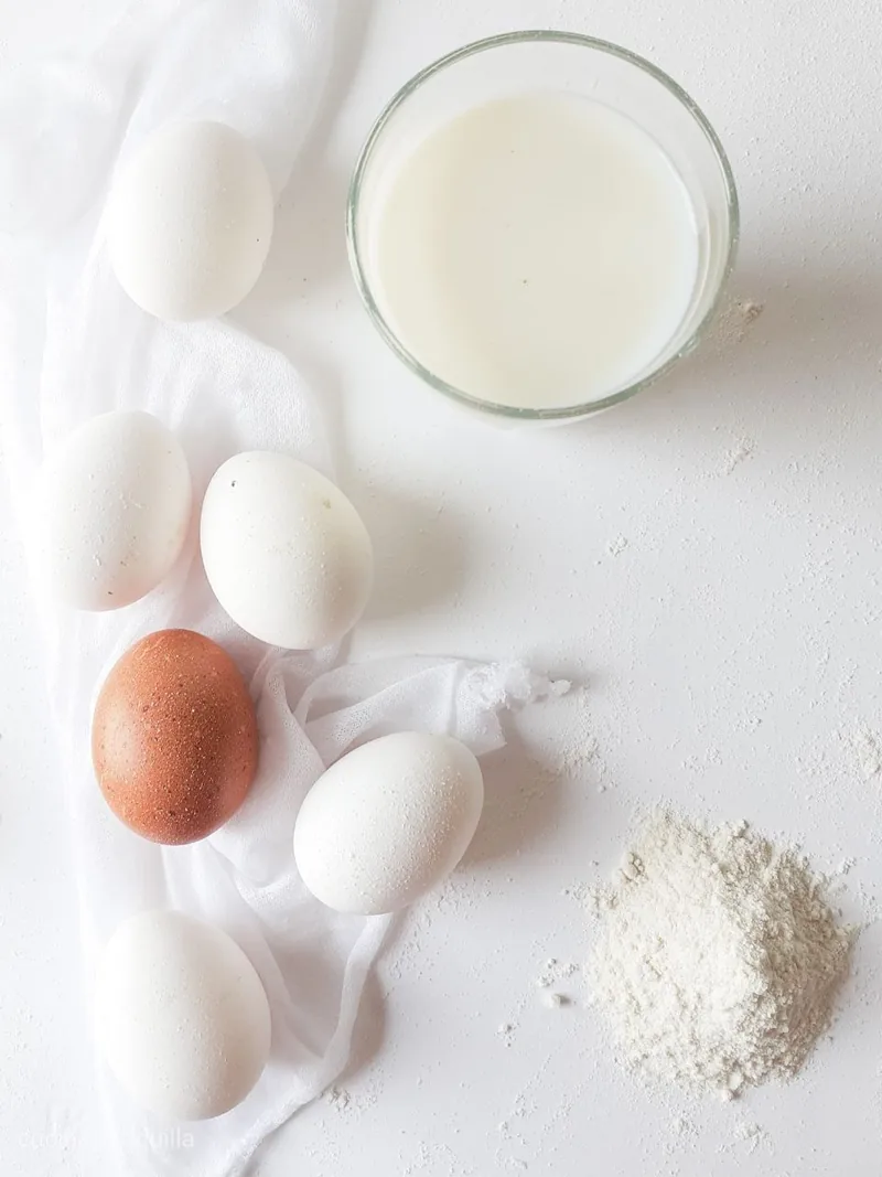 Uova fresche su un telo di cotone accanto a un bicchiere di latte e a una manciata di farina